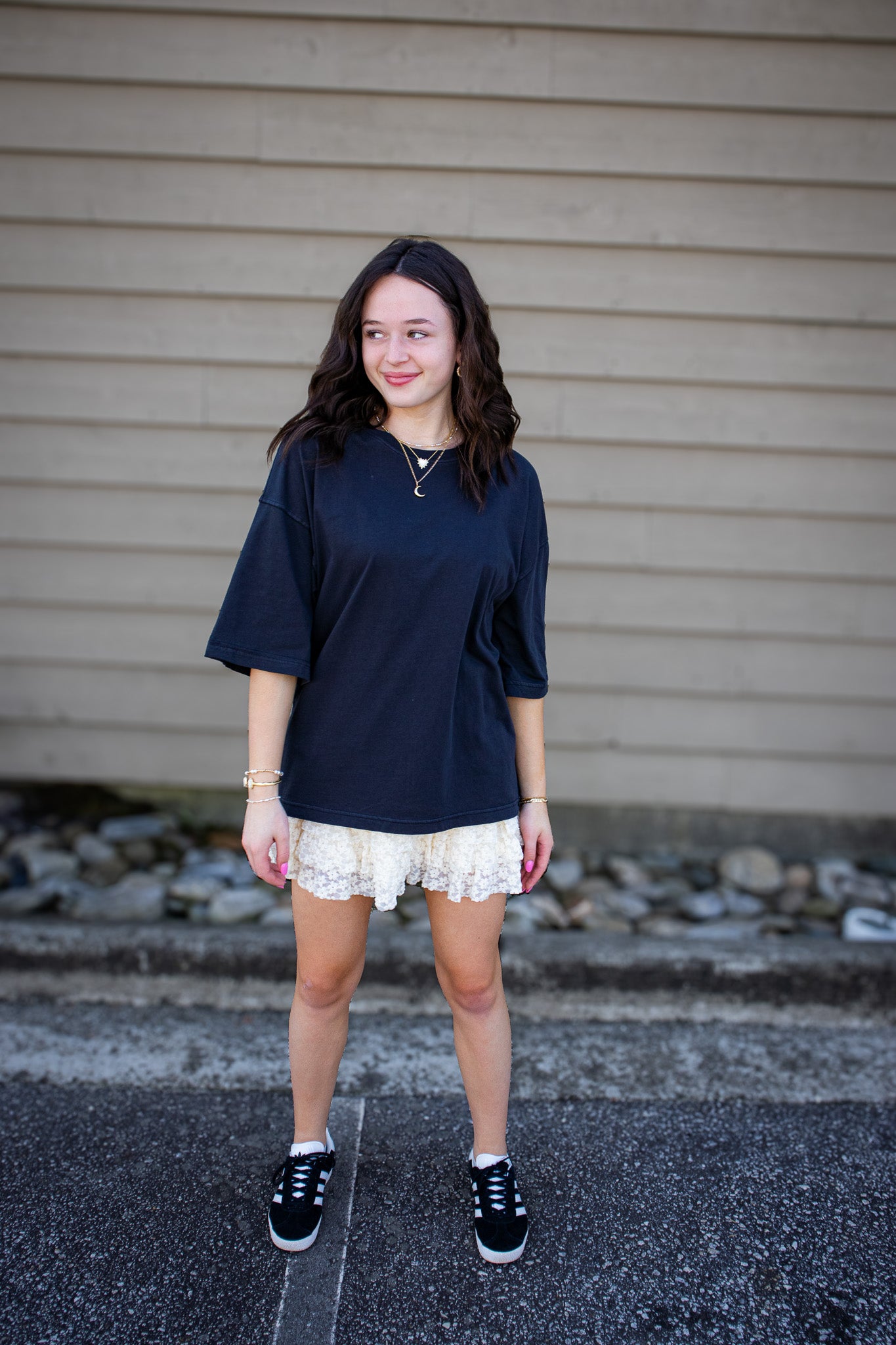 Woman wearing a black oversized tee and white lace shorts standing in front of a beige wall