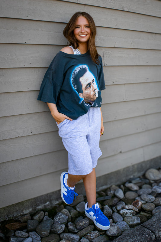 Woman wearing a graphic t-shirt and shorts standing against a wooden wall.