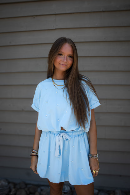 Young girl wearing a light blue set standing against a neutral background