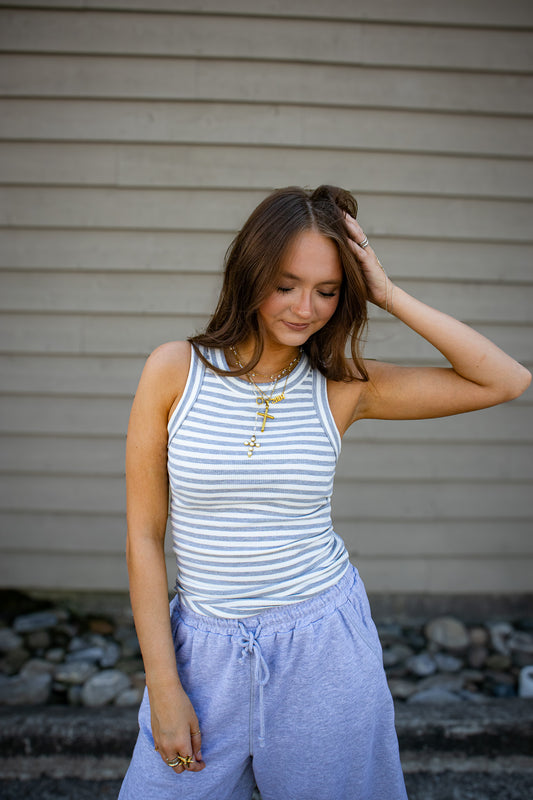Woman wearing a striped tank top and grey pants standing against a beige wall.