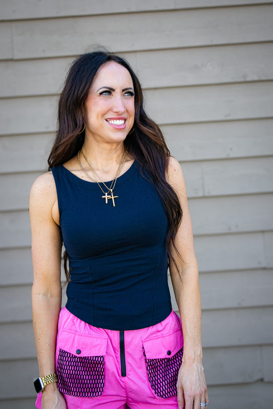 Woman wearing a black tank top and pink shorts standing against a beige wall.