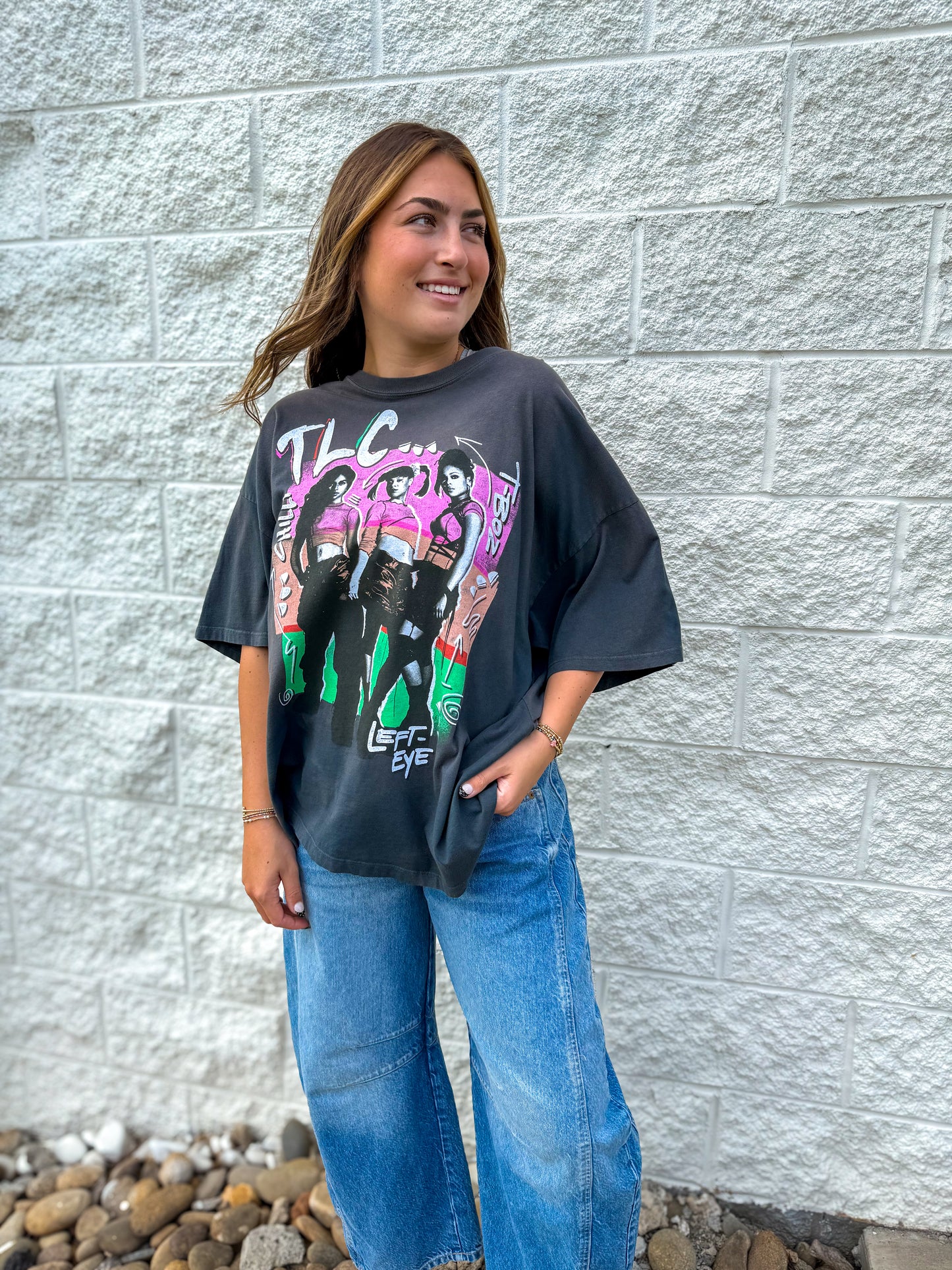 Person wearing a graphic t-shirt with colorful design against a gray brick wall.
