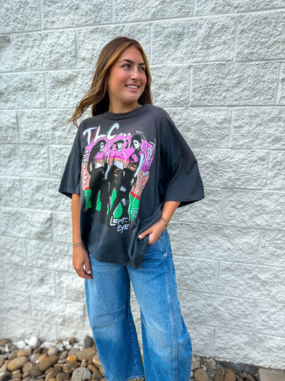 Person wearing a graphic t-shirt with colorful design against a gray brick wall.
