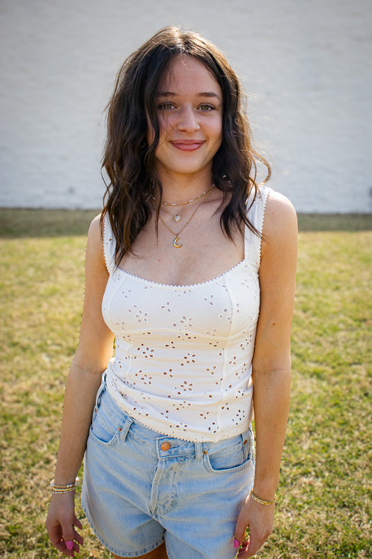 Woman wearing a white sleeveless top with cut-out details and light blue shorts outdoors.