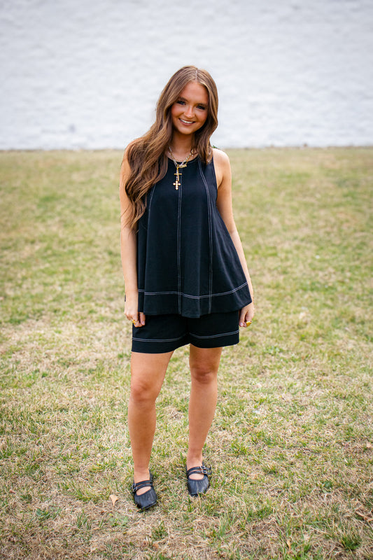 Woman wearing a black sleeveless top and shorts standing in a grassy field.