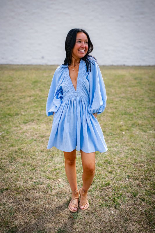 Woman wearing a blue dress standing in a grassy area with a white wall background