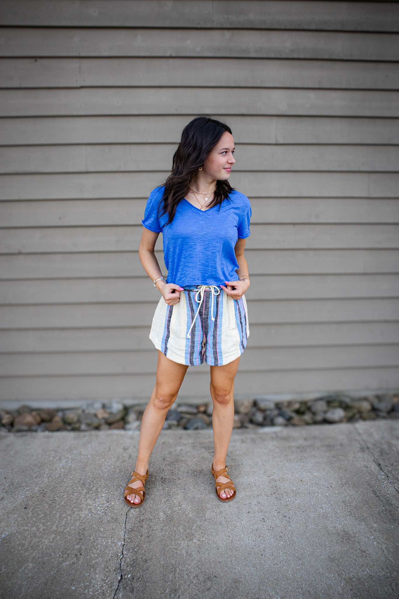 Woman wearing a blue v-neck tee and striped shorts standing against a gray wall.