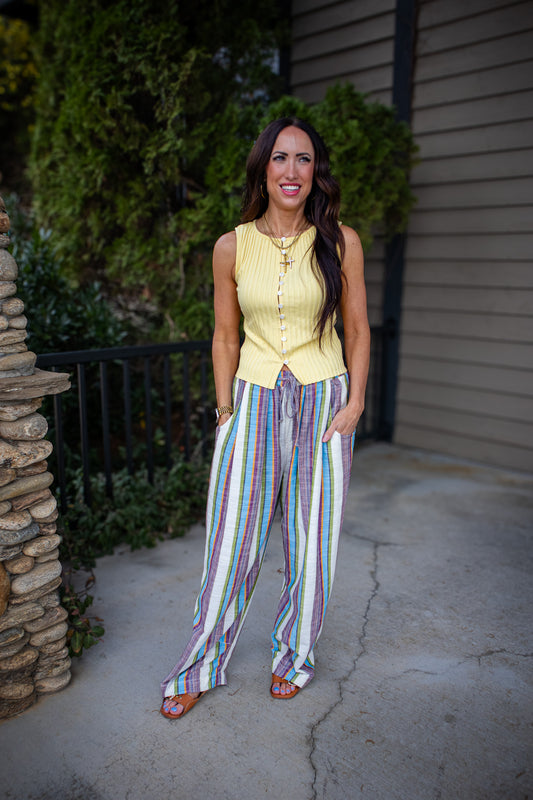Woman wearing a yellow sleeveless top and colorful striped pants standing outdoors.
