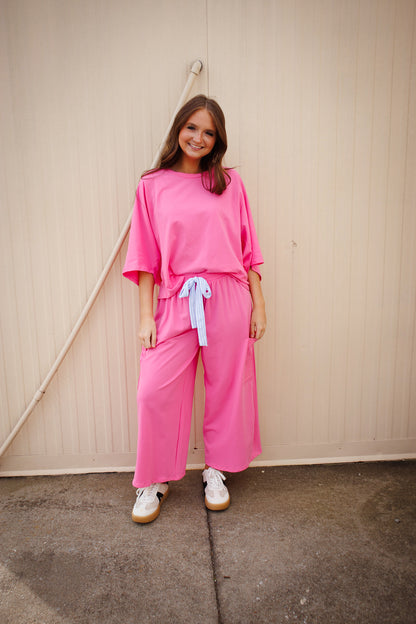 Woman wearing a bright pink outfit with a white wall background