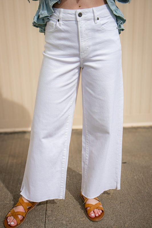 Person wearing white wide-leg jeans with a beige background
