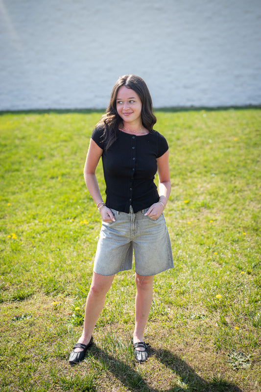 Person wearing a black shirt and light shorts standing on grass with a white wall in the background