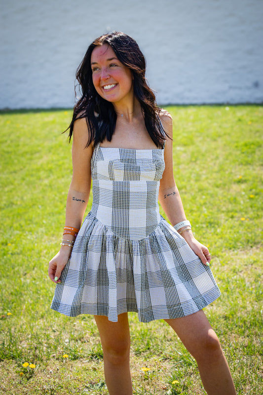Woman wearing a plaid dress standing in a grassy area with a white wall in the background