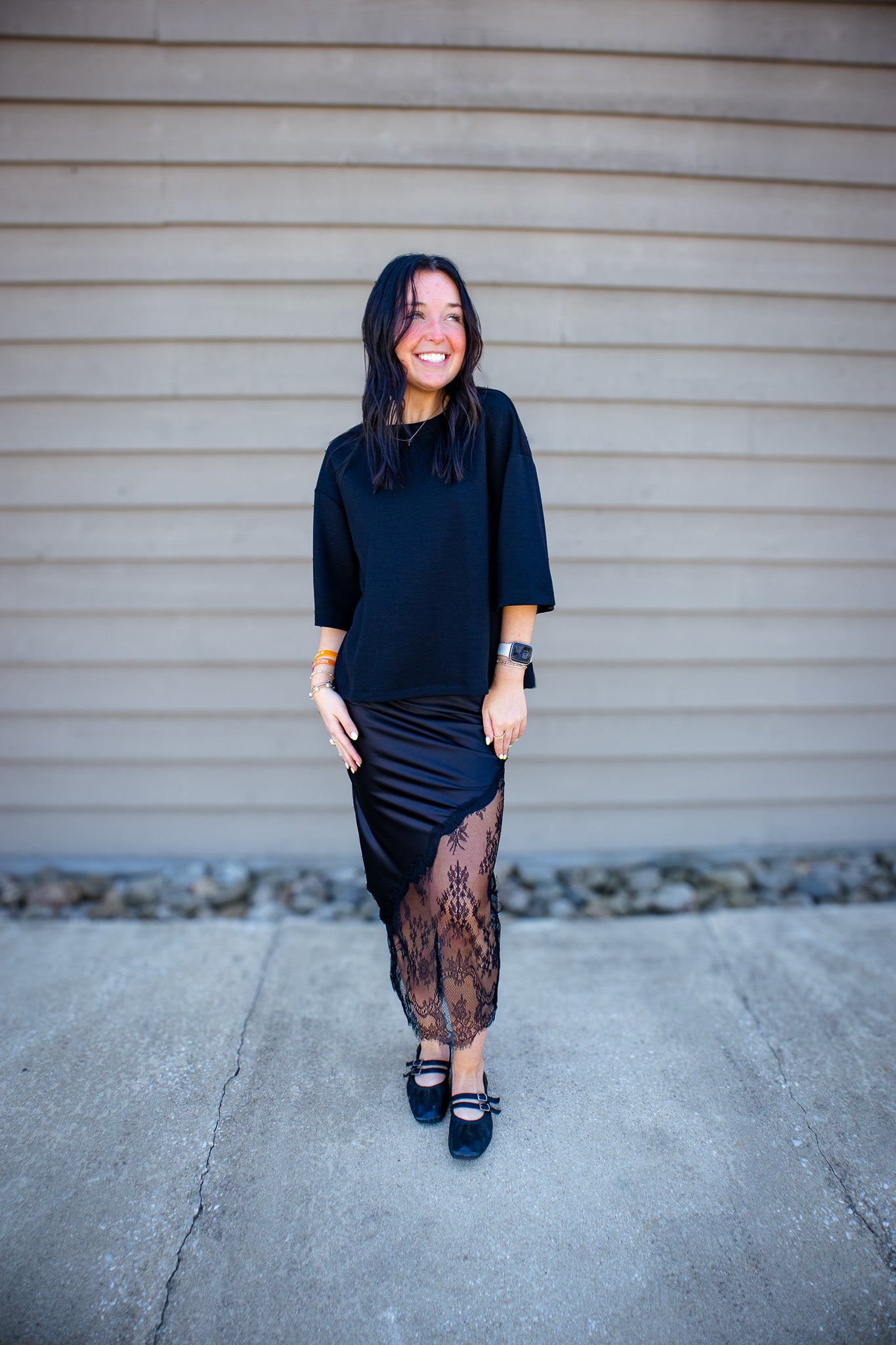 Woman wearing a black outfit with sheer details against a beige wall.