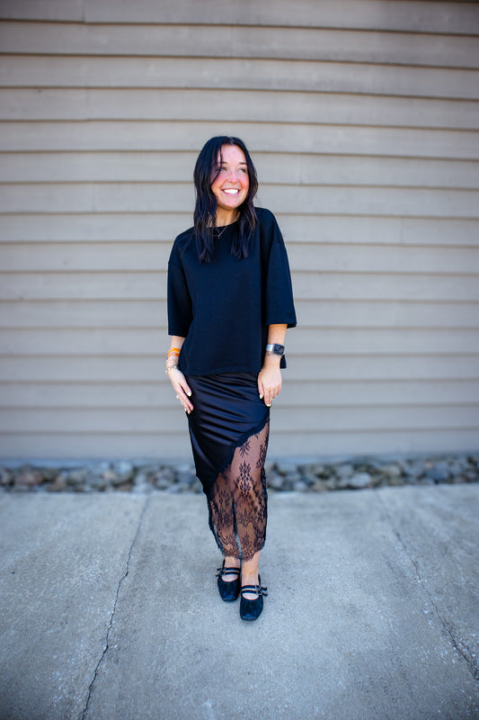 Woman wearing a black outfit with sheer details against a beige wall.