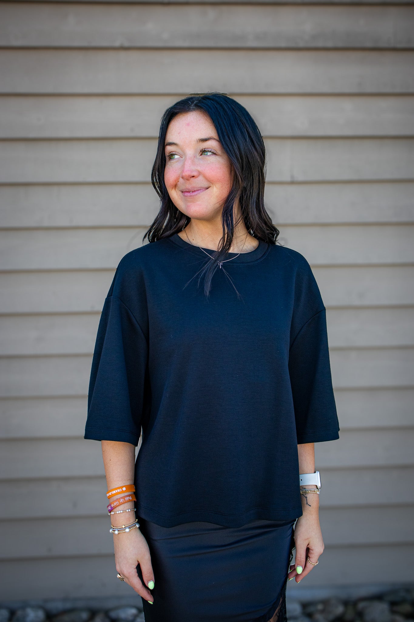 Woman wearing a black top standing against a beige wall.