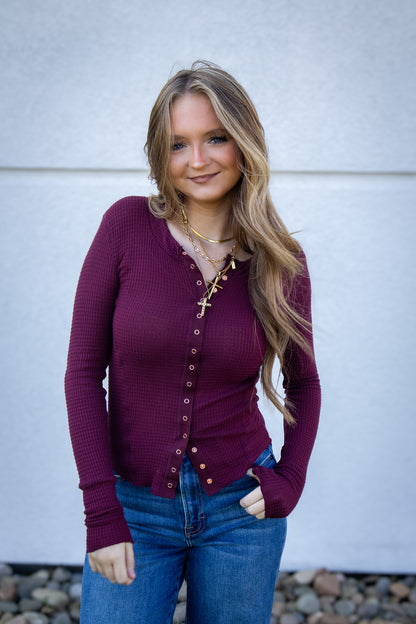 Woman wearing a purple cardigan and blue jeans against a white wall.
