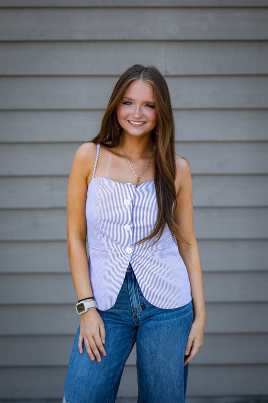 Woman wearing a black and white striped tank top and jeans standing against a gray wall.