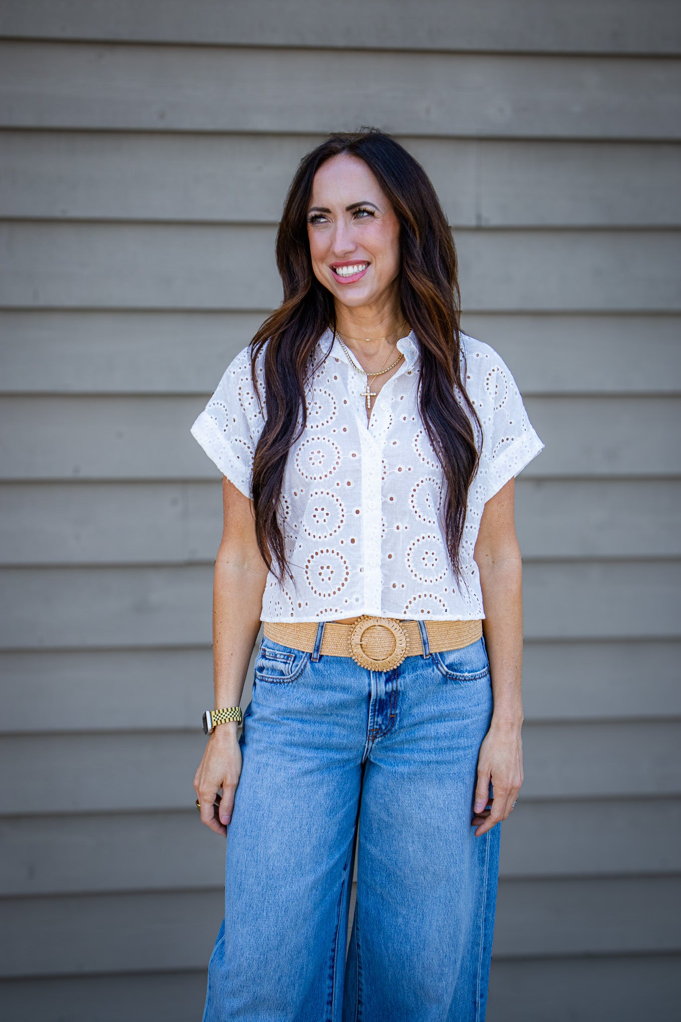 Woman wearing a white blouse and blue jeans standing against a gray wall.
