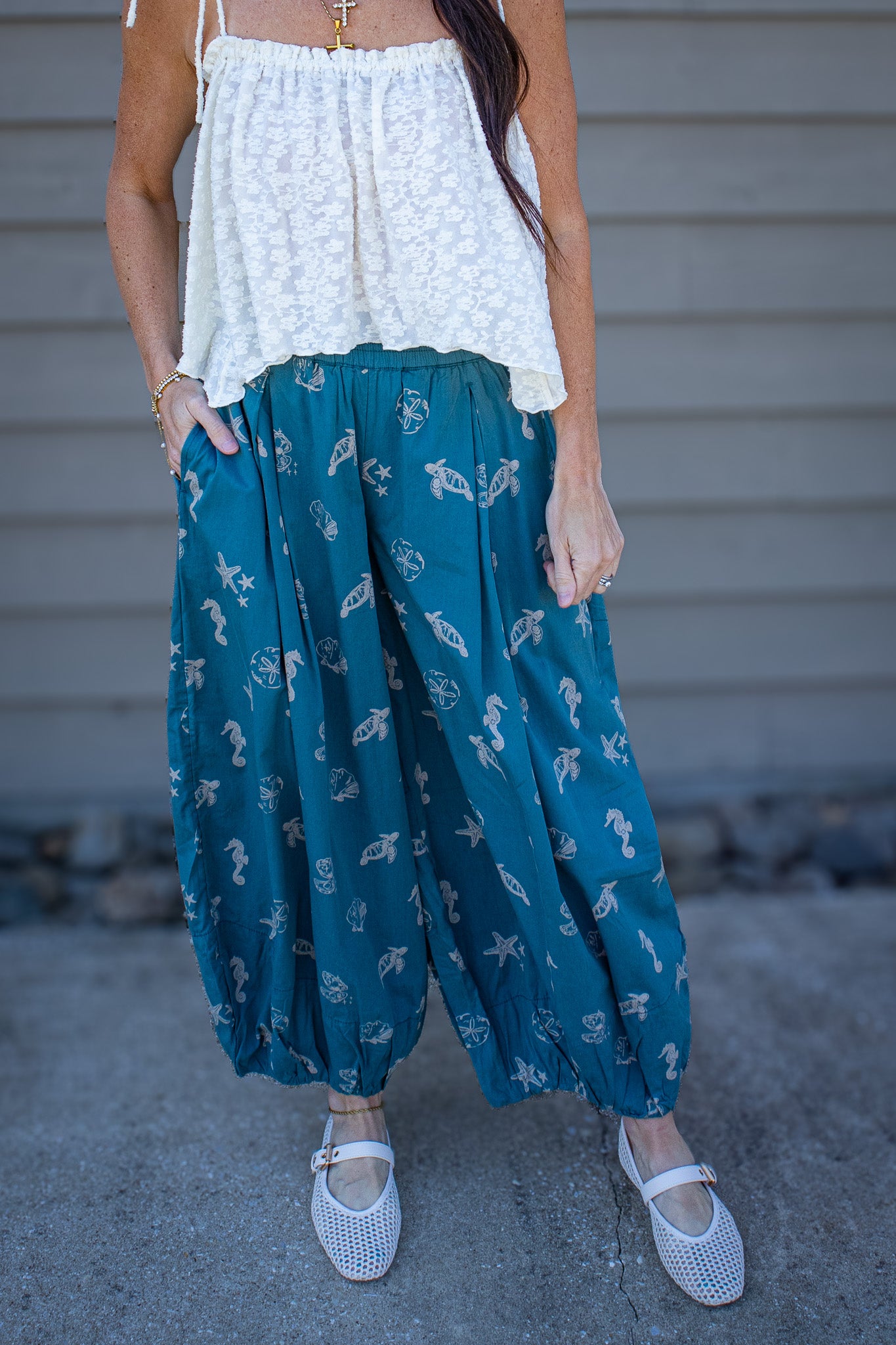 Person wearing a white top and teal patterned pants standing against a neutral background