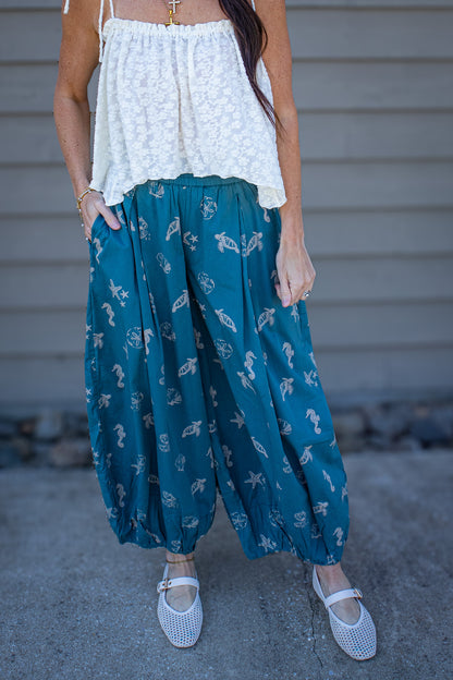 Person wearing a white top and teal patterned pants standing against a neutral background