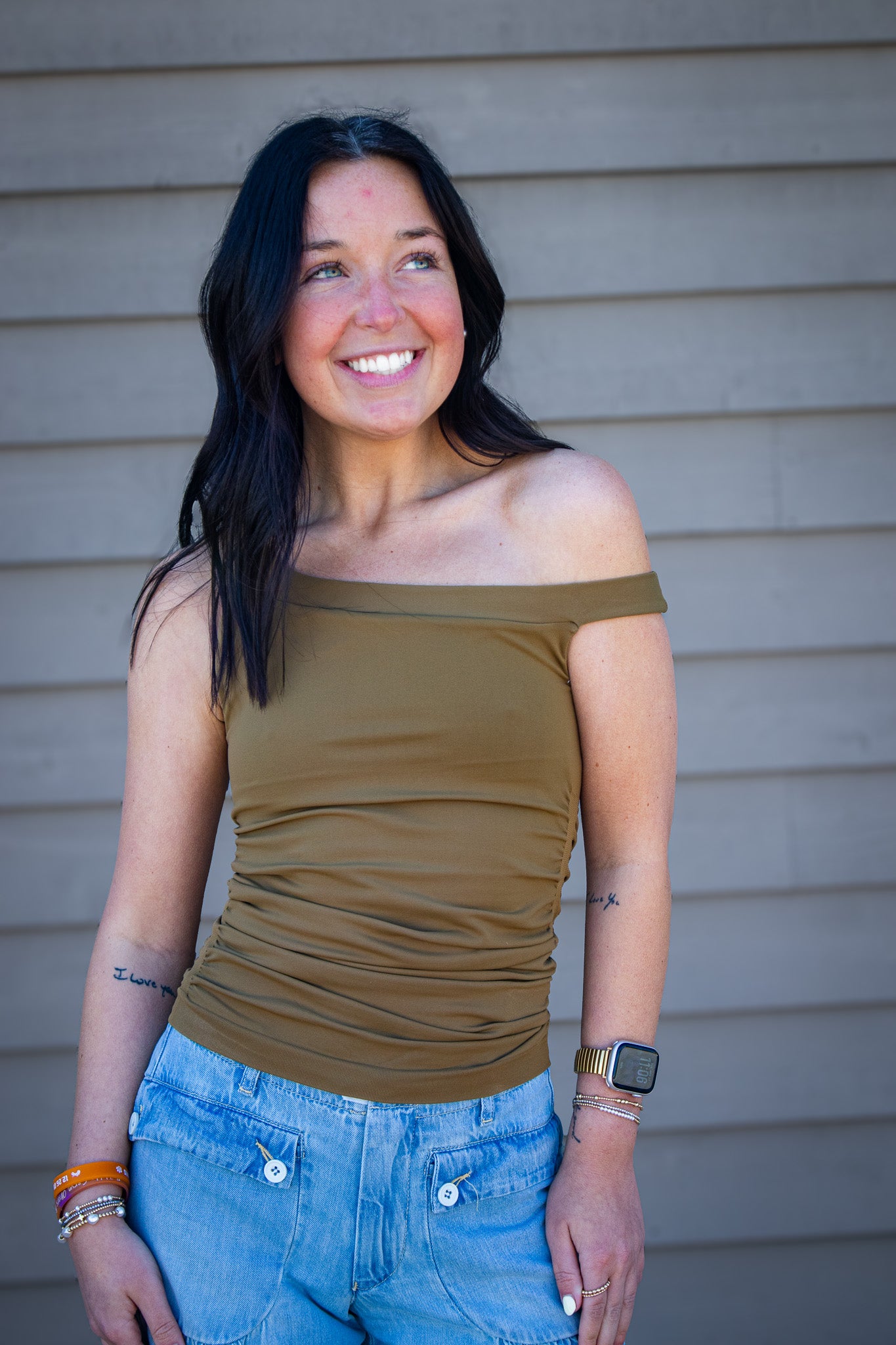 Woman wearing olive green ruched off shoulder top with light wash wide leg jeans, trendy casual outfit styled for everyday wear, boutique fashion look outdoors