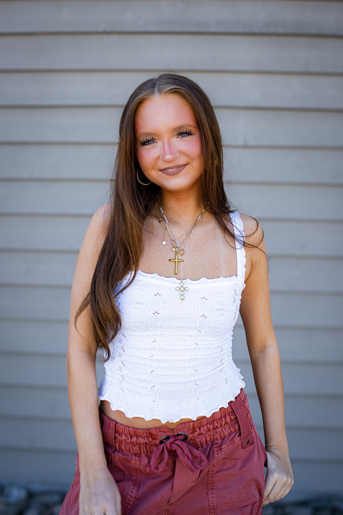 Woman wearing white lace trim fitted tank top with rust wide leg cargo pants, trendy casual boutique outfit styled with layered gold necklaces outdoors