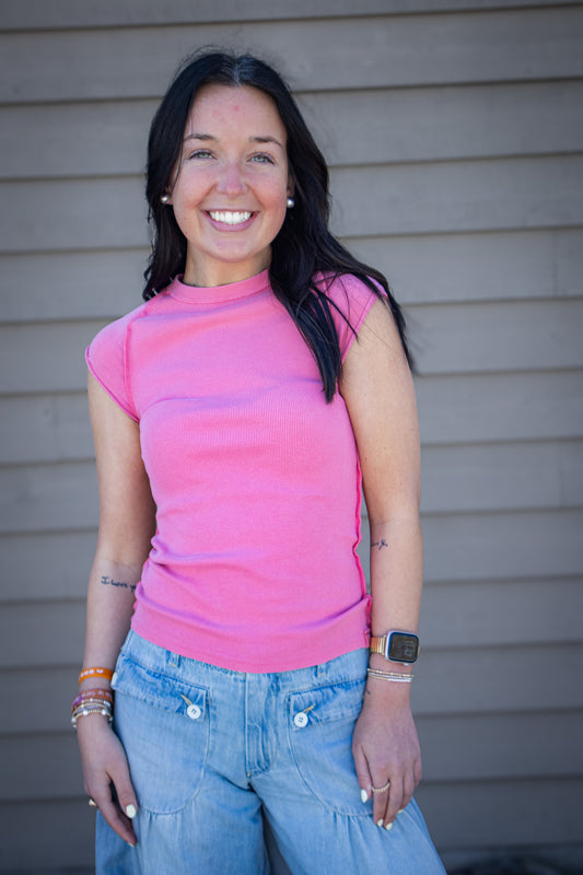 Woman wearing bright pink fitted cap sleeve top with light wash wide leg jeans, casual trendy outfit styled for everyday wear, boutique fashion look outdoors