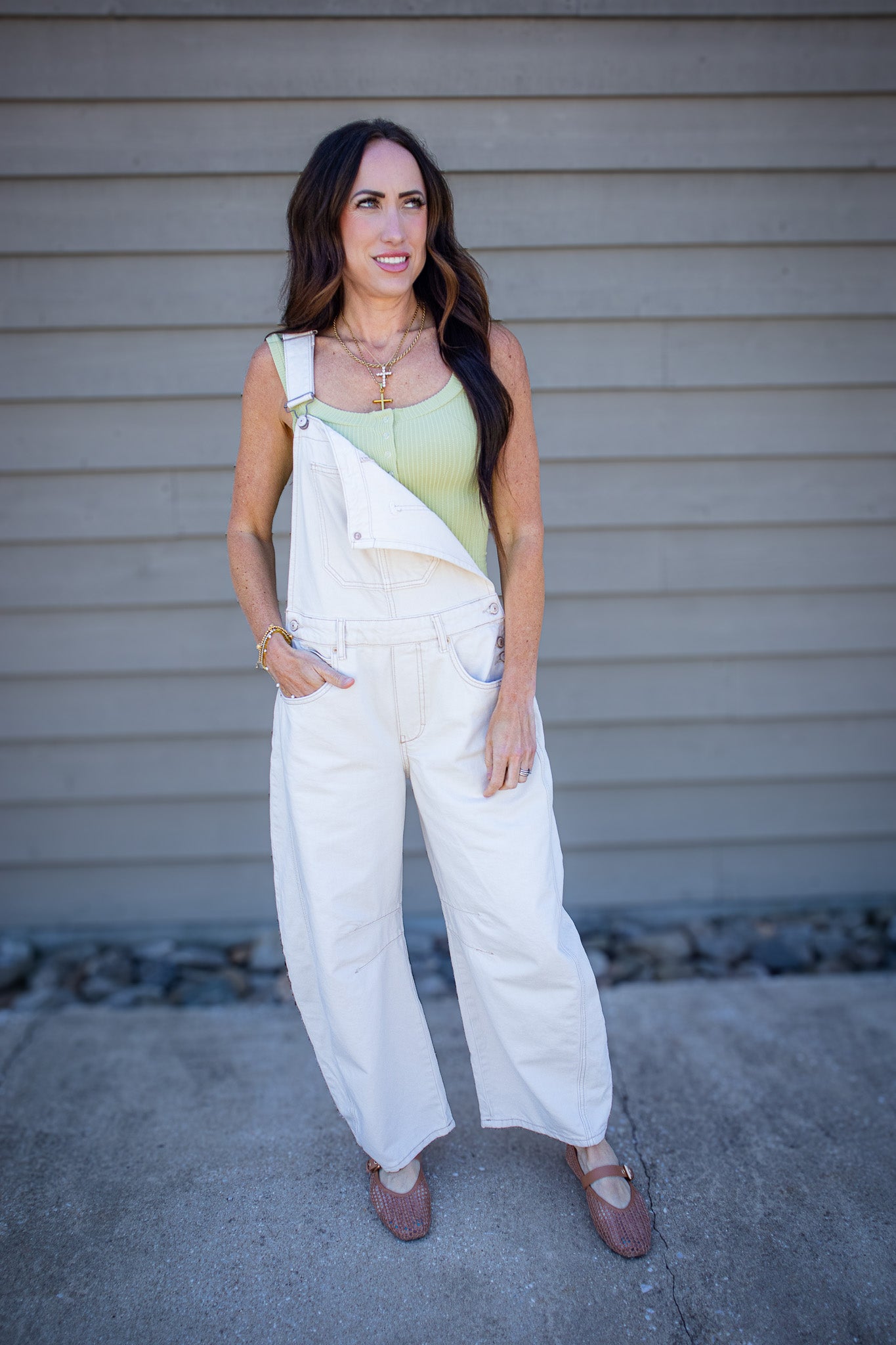 Cream wide-leg denim overalls styled with a light green ribbed tank top and woven flats for an effortless casual boutique outfit. Relaxed neutral overalls with adjustable straps, front pocket detail, and laid-back summer styling perfect for everyday wear, weekend outings, and vacation looks.