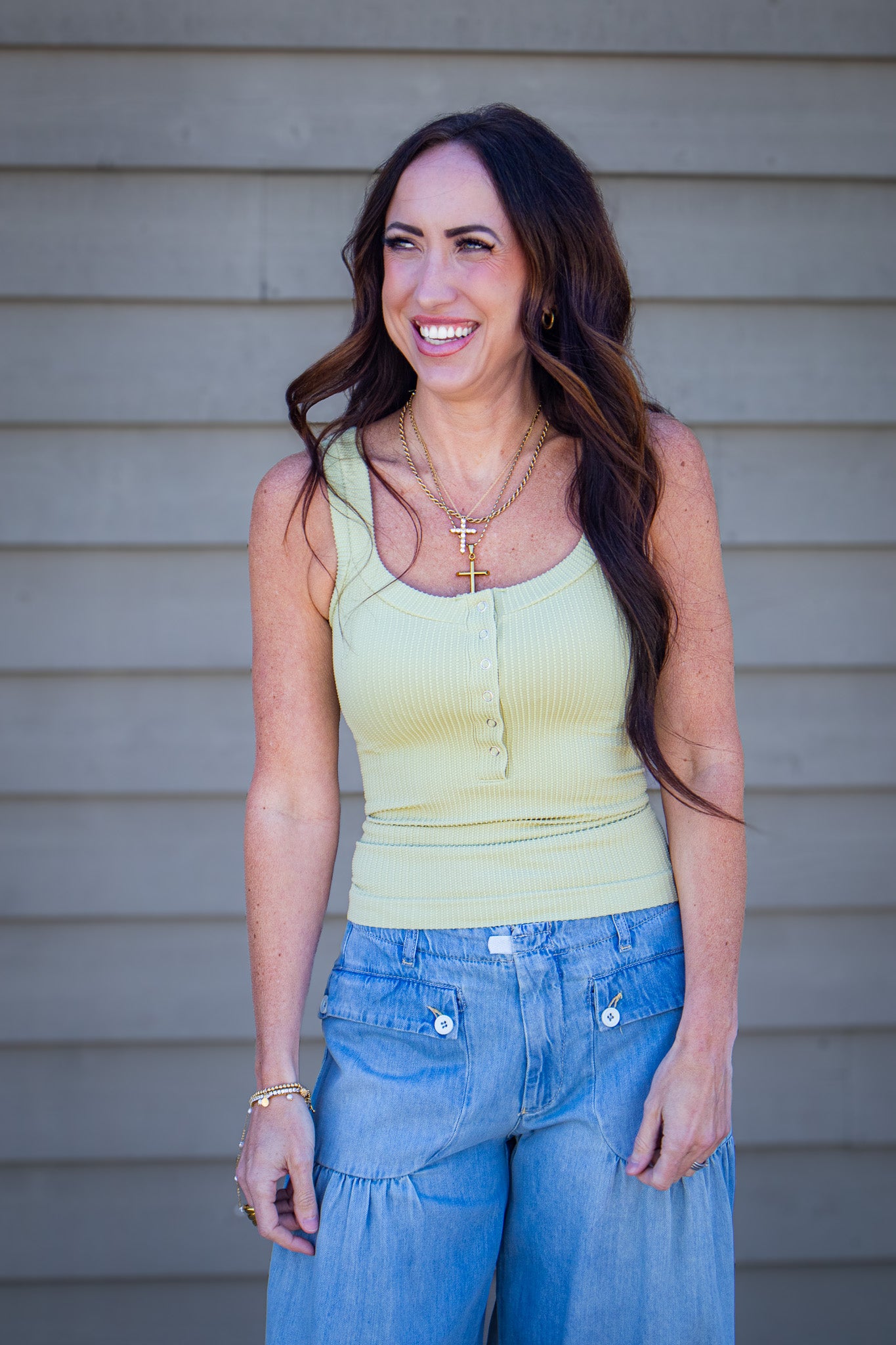 Woman wearing light green ribbed sleeveless tank top with light wash wide leg jeans, casual spring outfit styled with layered gold necklaces, trendy boutique fashion look outdoors