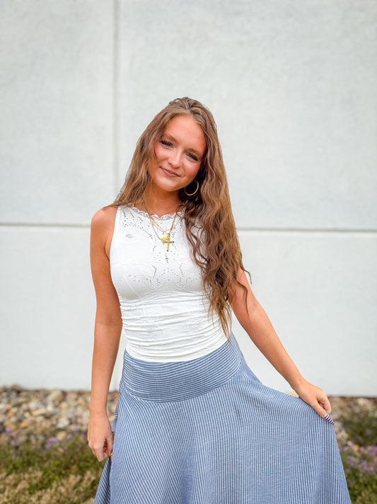Woman wearing a white top and blue skirt against a white wall.