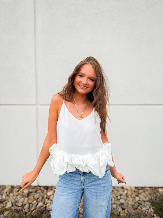Woman wearing a white ruffled top and blue jeans against a light gray wall.