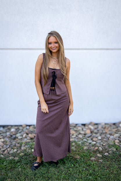 Woman wearing a brown polka-dot tank and matching skirt standing on grass with a white wall in the background