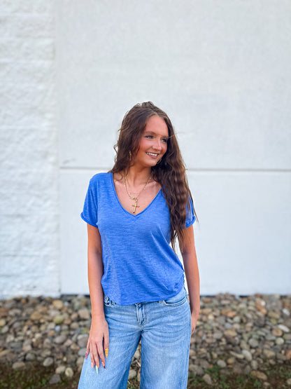 Woman wearing a blue v-neck tee and jeans standing against a white wall.