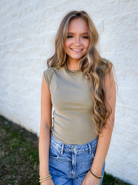 Woman wearing a green sleeveless top and blue jeans against a white wall.