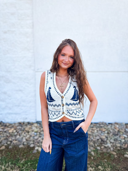 Woman wearing a sleeveless patterned top and blue jeans against a white wall.