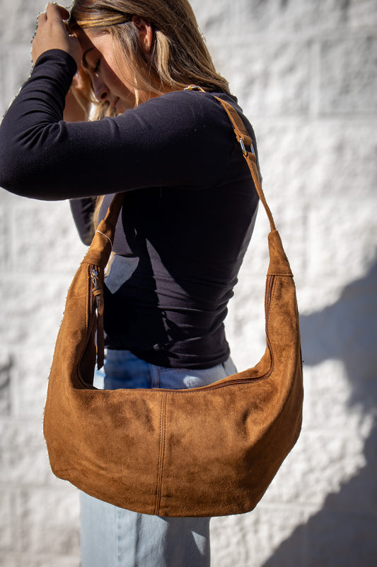 Woman carrying a brown shoulder bag against a white textured wall