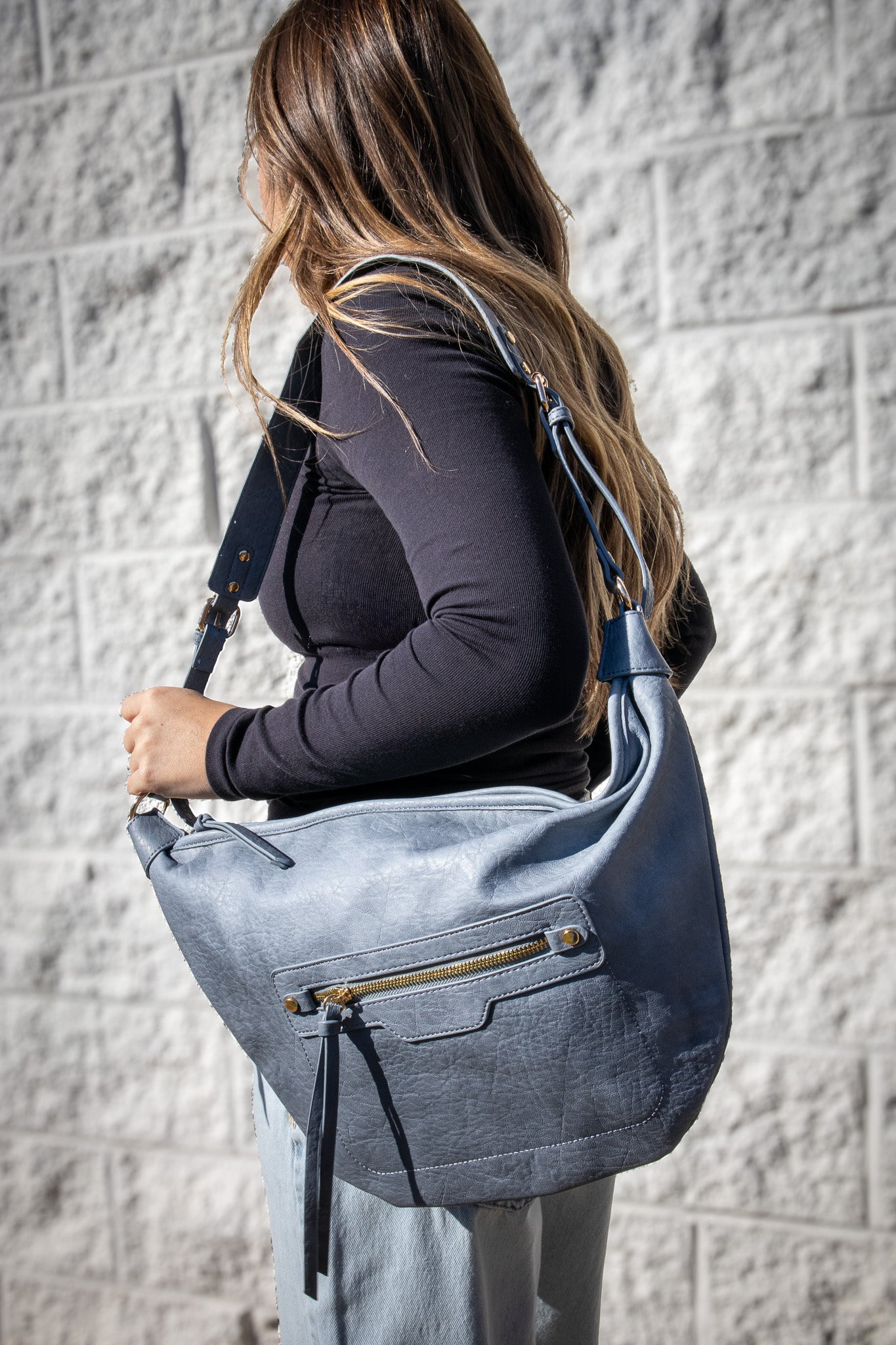 Woman carrying a blue shoulder bag against a gray brick wall.
