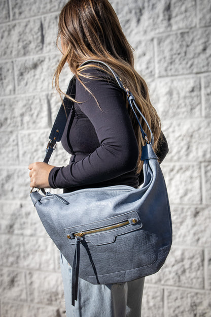 Woman carrying a blue shoulder bag against a gray brick wall.