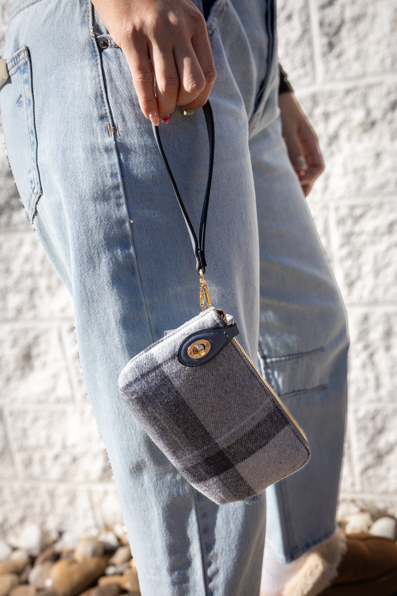 Person holding a plaid patterned pouch with a white textured wall background