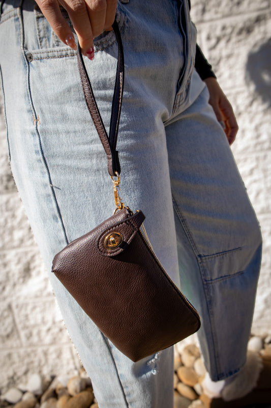 Minimal brown leather wristlet with strap and gold hardware, styled with light-wash jeans