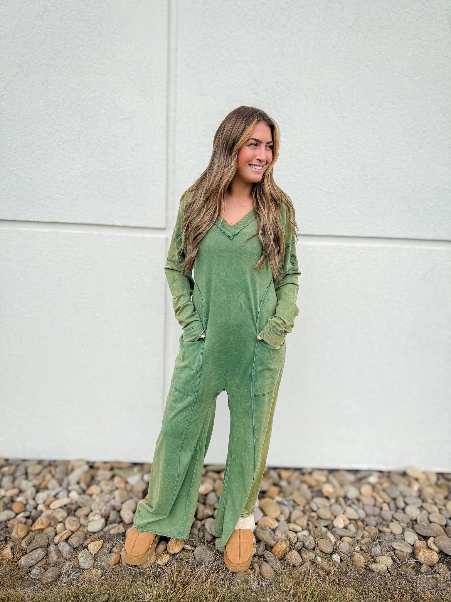 Woman wearing a green jumpsuit standing on a gravel path with a white wall background