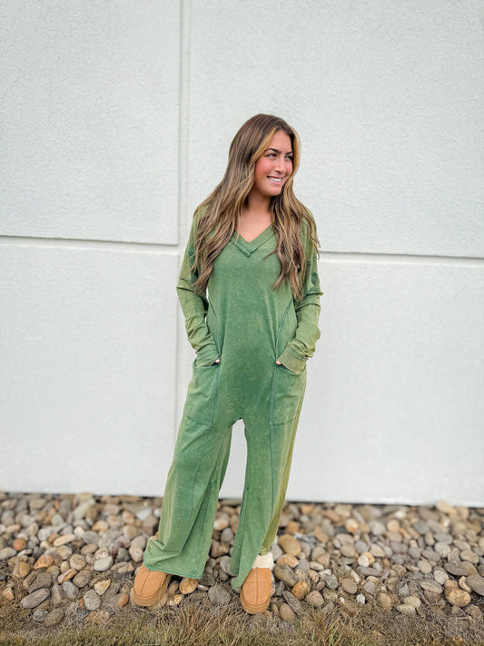 Woman wearing a green jumpsuit standing on a gravel path with a white wall background