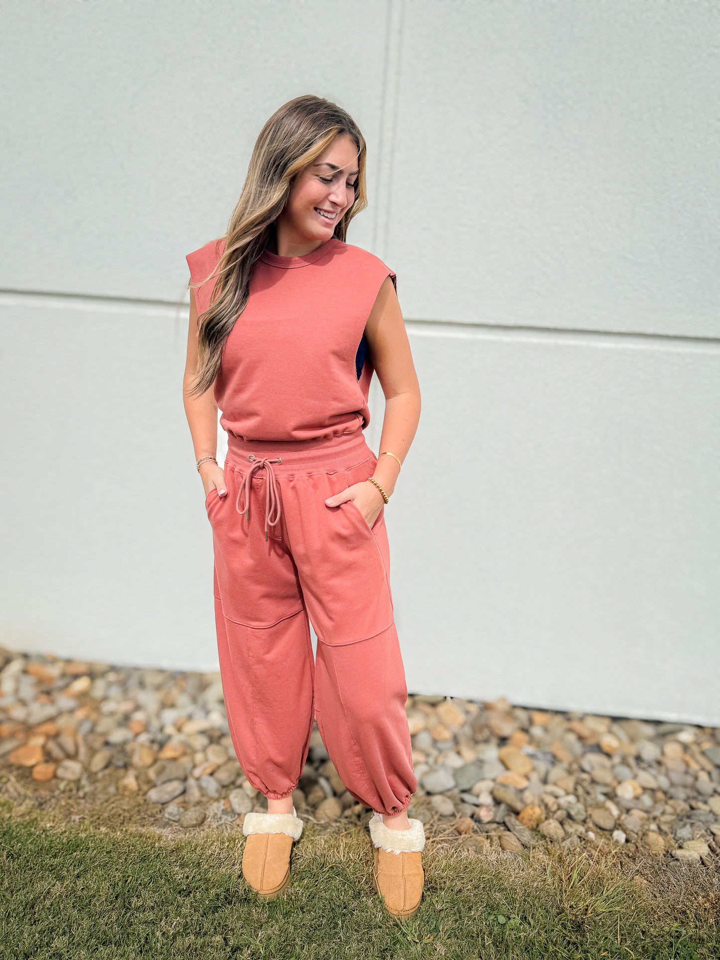 Woman wearing a pink outfit standing outdoors on a grassy area with a white wall in the background.
