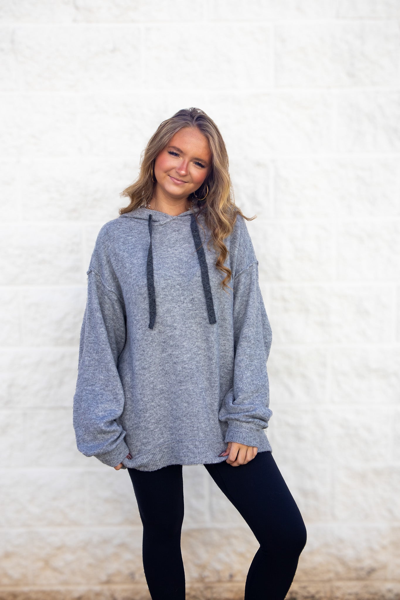 Woman wearing a gray hoodie and black leggings against a white background