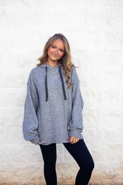 Woman wearing a gray hoodie and black leggings against a white background
