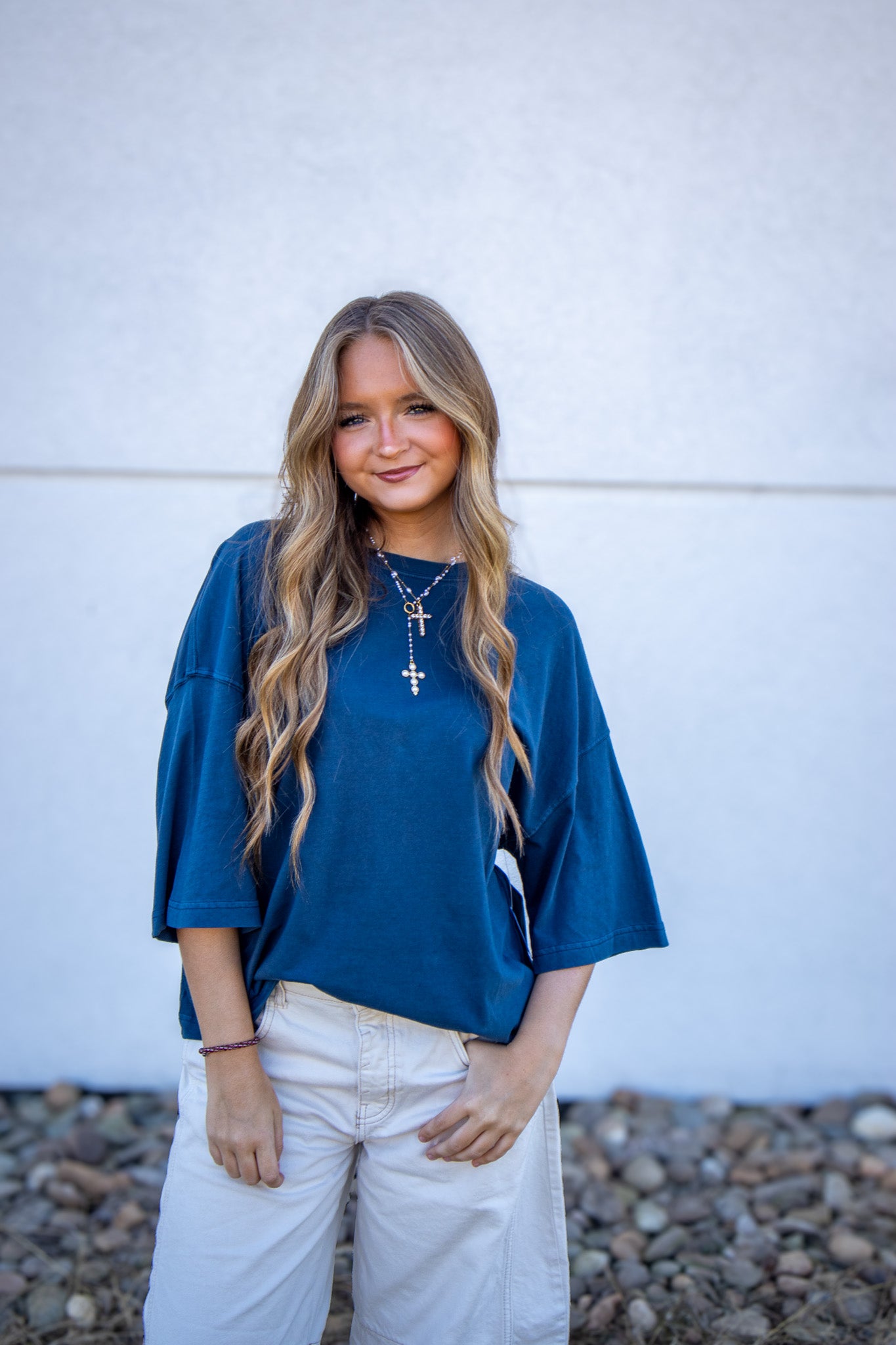 Woman wearing an oversized blue tee and white barrel leg jeans standing against a white wall.