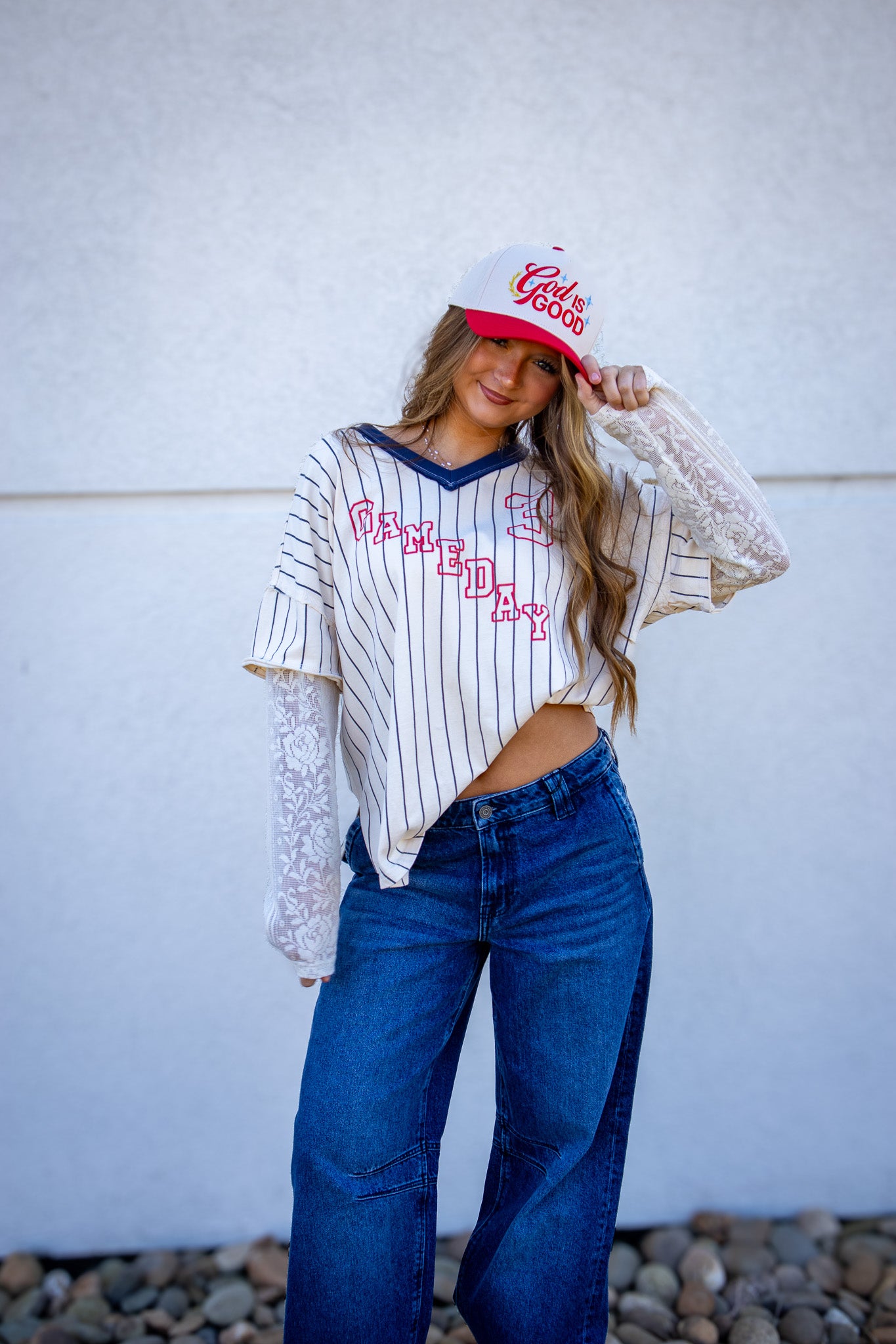Woman wearing a striped shirt, jeans, and a cap with text against a white wall.