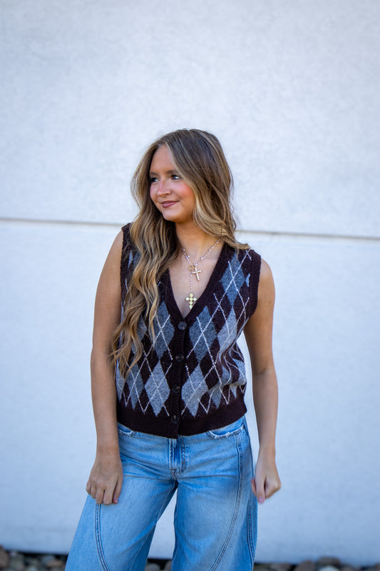 Woman wearing a patterned sweater vest and jeans against a white wall