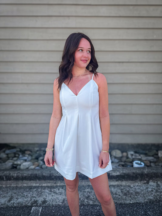 Woman wearing a white dress standing on steps with a neutral background