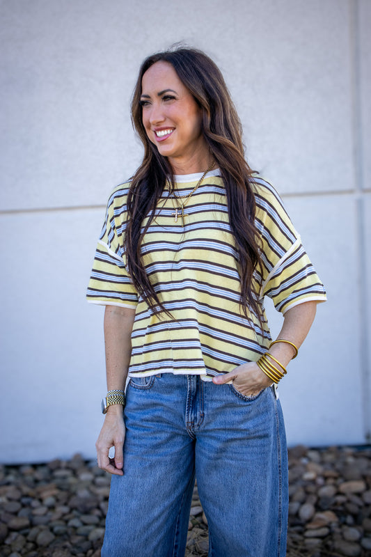 Woman wearing a yellow and blue striped shirt and blue jeans standing against a white wall.